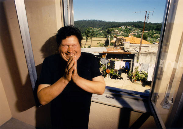 Rosa Coelho praises God that she no longer has to live in the shack visible through the window behind her in Cunha, Portugal. (2001)